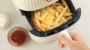Kraukšķīgi frī kartupeļi airfryer friterī ar divām mērcēm uz galda.