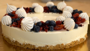Gaisīga jogurta kūka ar ogām un bezē cepumiem uz zelta paplātes.