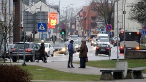 Cilvēki uz ietves un automašīnas satiksmē nelielā pilsētā ziemas laikā