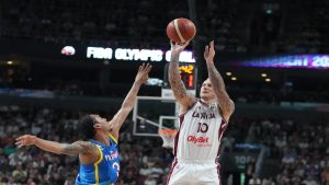 Latvijas basketbolists met bumbu grozā spēles laikā pretinieku komandas spēlētāja klātbūtnē.