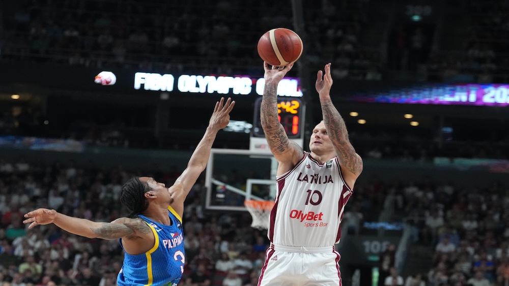 Latvijas basketbolists met bumbu grozā spēles laikā pretinieku komandas spēlētāja klātbūtnē.