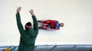 Latvijas kamaniņu braucējs sacensību laikā Siguldas trasē, līdzjutējs priecājas trases malā.