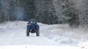 Traktors brauc pa sniegotu autoceļu meža vidū Mazsalaca-Staicele posmā.