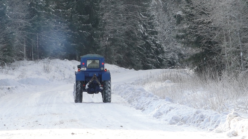 Traktors brauc pa sniegotu autoceļu meža vidū Mazsalaca-Staicele posmā.