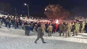 Cilvēki un jaunsargi pie ugunskura barikāžu piemiņas pasākumā ziemas vakarā.