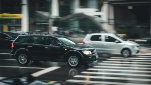 Automobiļi uz pilsētas ielas, šķērsojot gājēju pāreju mitrā laikā.