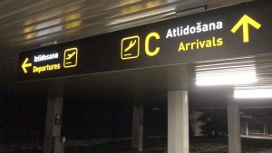 Norādes zīme Rīgas lidostas teritorijā ar uzrakstiem "Izlidošana" un "Atlidošana".