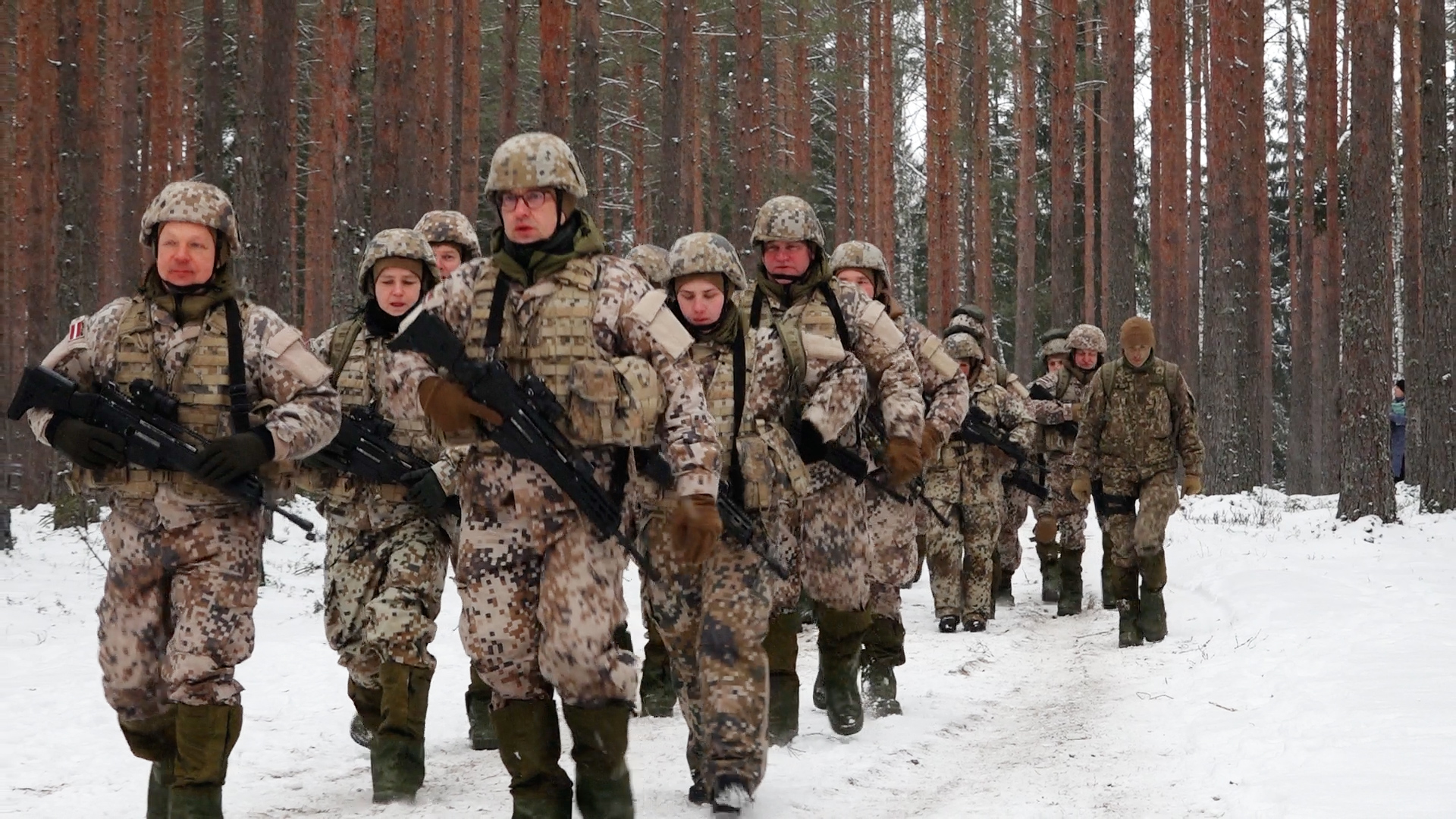 Latvijas rezervistu apmācības ziemā, karavīri soļo pa sniegotu mežu.