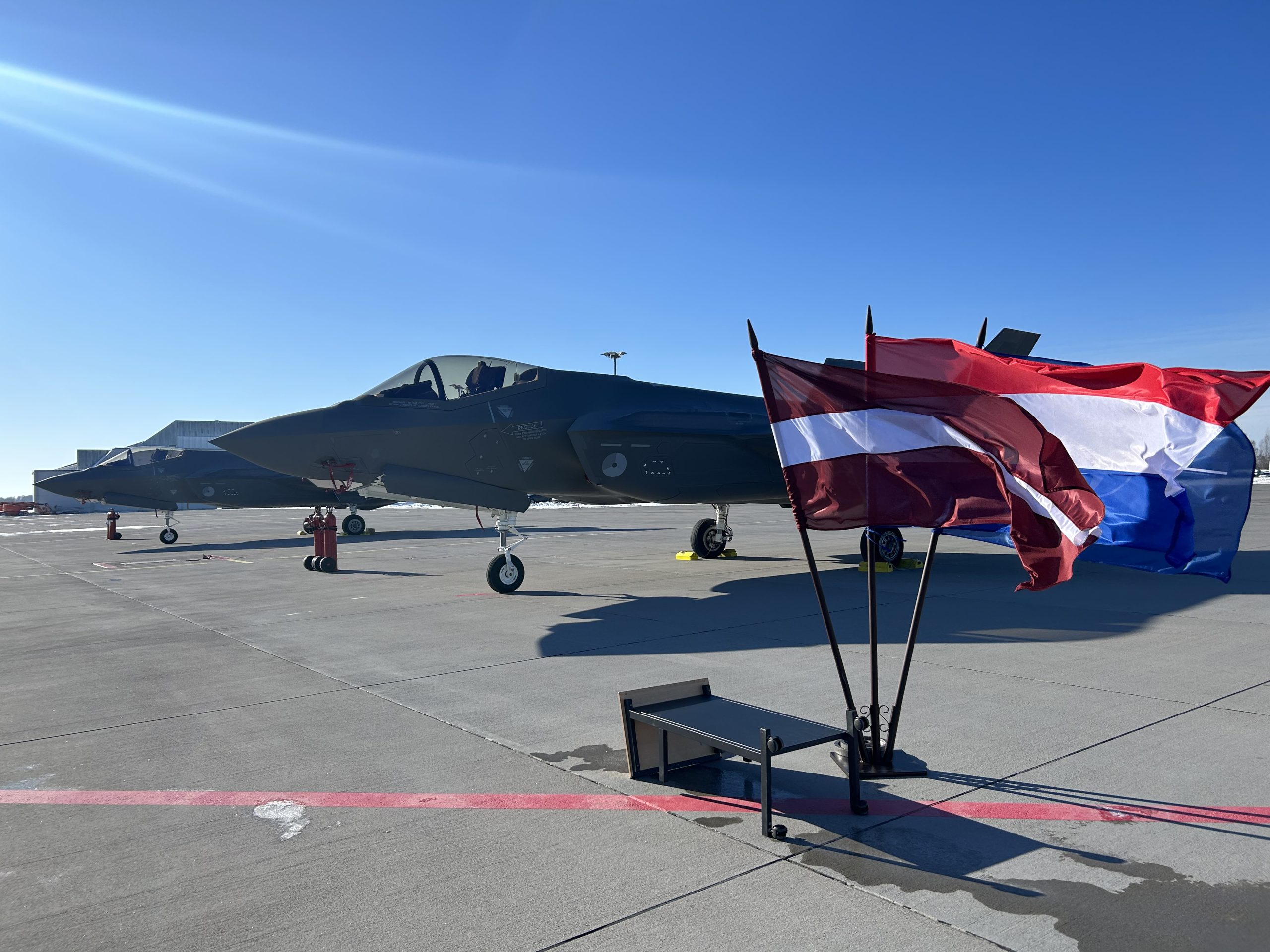 Nīderlandes iznīcinātāji F-35 uz skrejceļa Lielvārdes militārajā bāzē ar Latvijas un Nīderlandes karogiem priekšplānā.