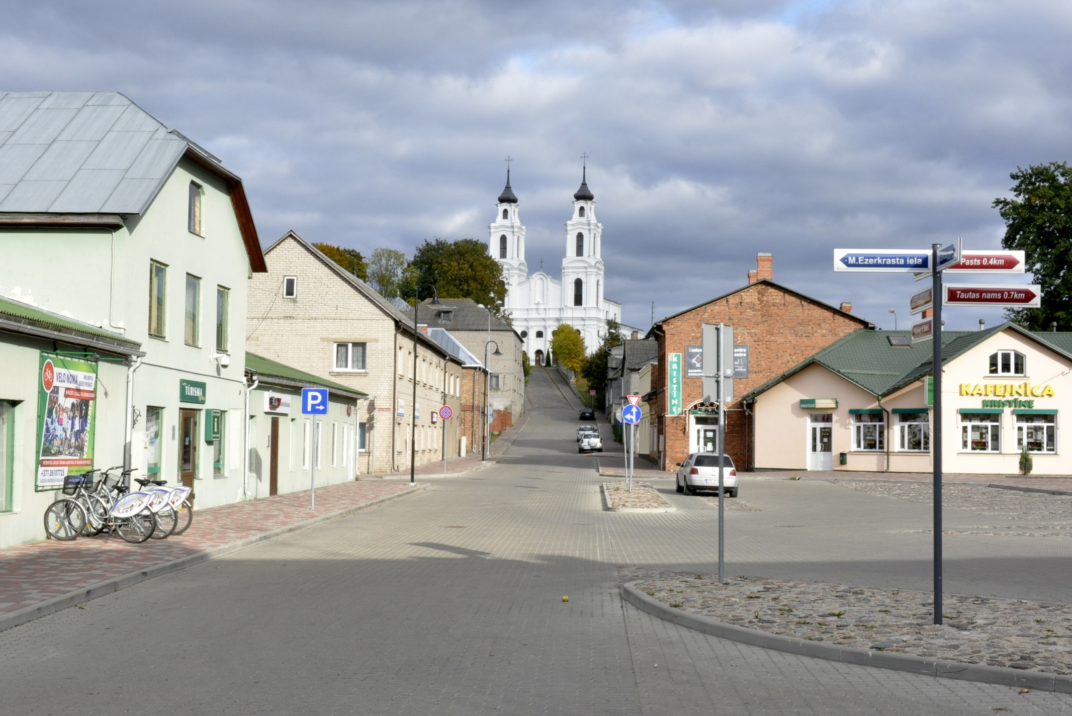 Skaista iela Ludzā ar skatu uz balto baznīcu kalnā, mākoņaina diena.