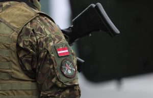 Latvijas karavīrs maskēšanās formā ar Latvijas karogu uz formas piedurknes.