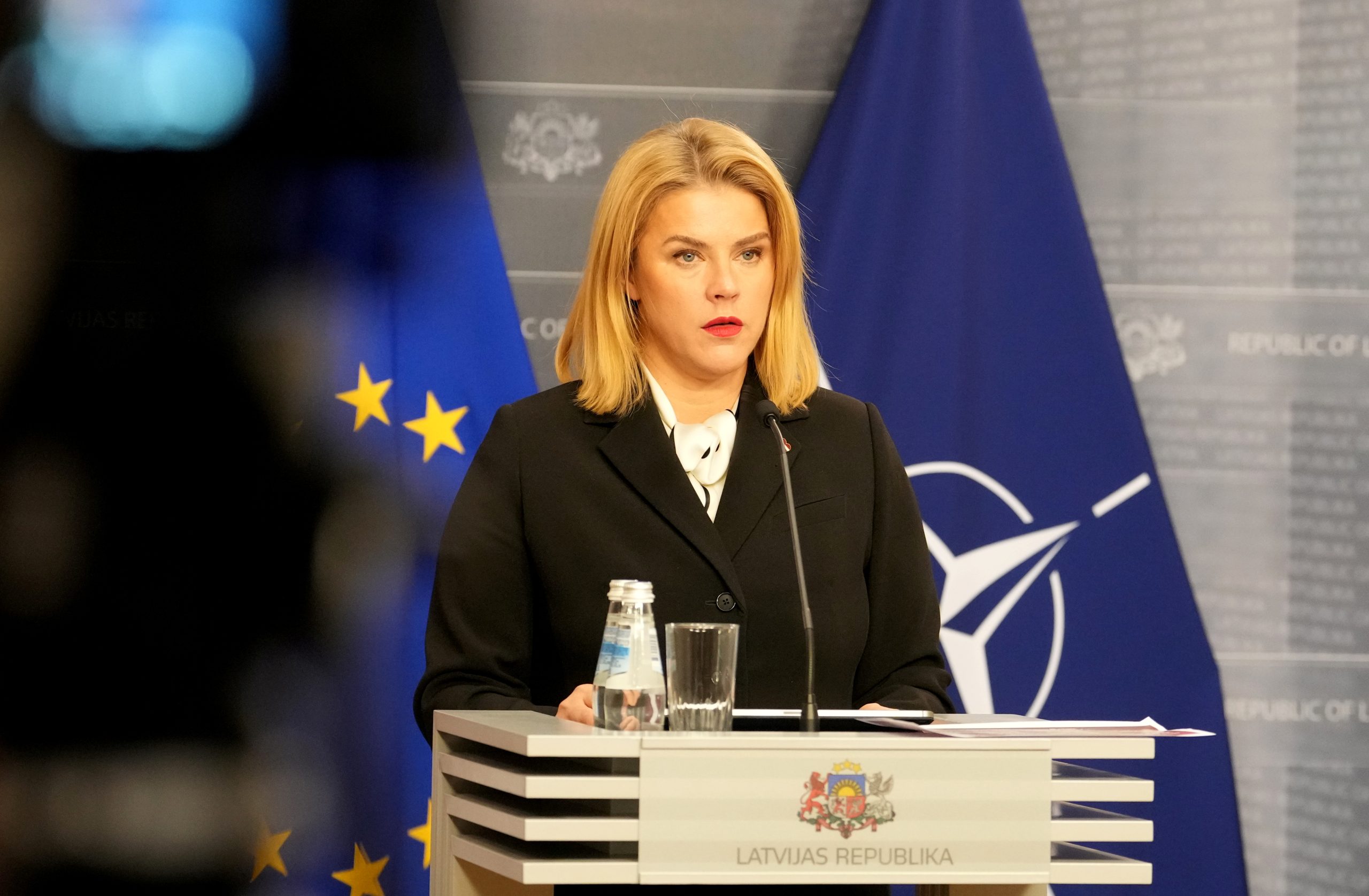 Ministru prezidente Evika Siliņa preses konferencē pie valdības tribīnes, fonā ES un NATO karogi.