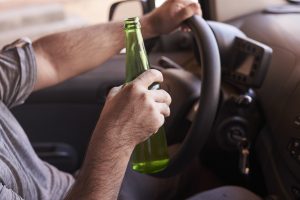 Vīrietis ar alus pudeli rokās, vadot automašīnu
