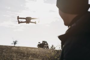 Vīrietis vēro dronu lidojumā dabas ainavā saulainā dienā.