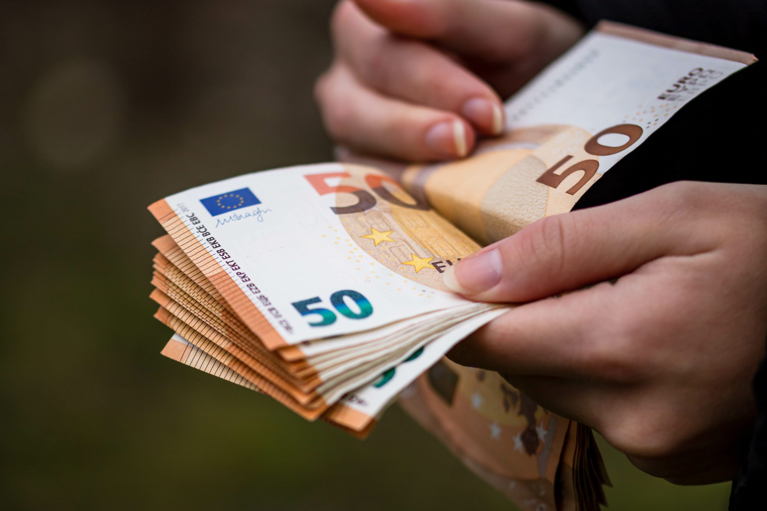 Rokas skaita 50 eiro banknotes, simbolizējot naudu un finanšu darījumus.