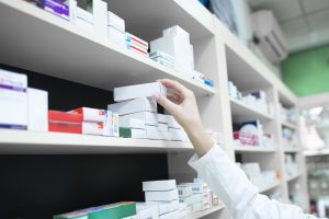Farmaceita roka, kas ņem medikamentu kārbiņu no aptiekas plaukta