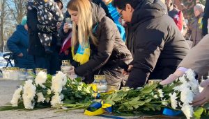 Cilvēki noliek ziedus un aizdedzina svecītes piemiņas pasākumā par Ukrainu.