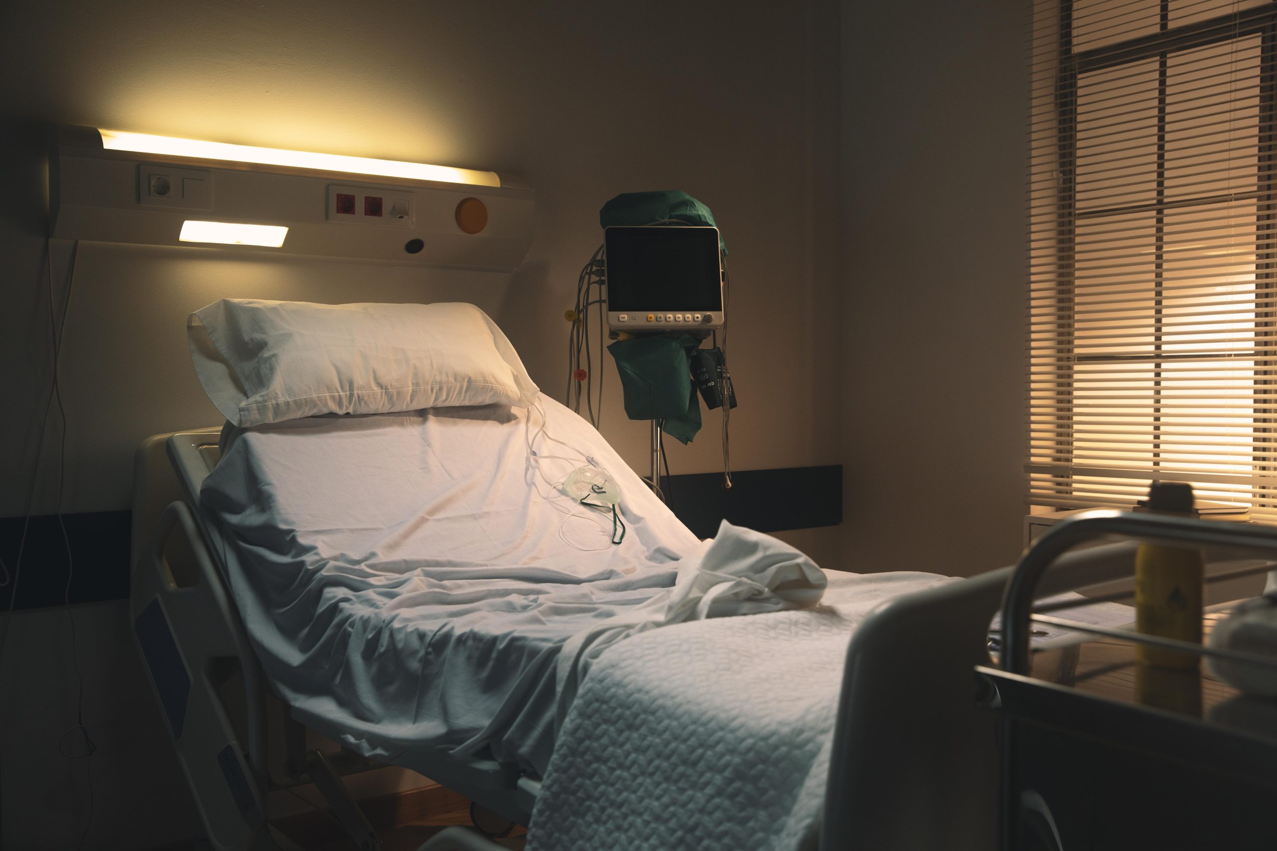 Tukša slimnīcas gulta ar medicīnas aprīkojumu blakus.