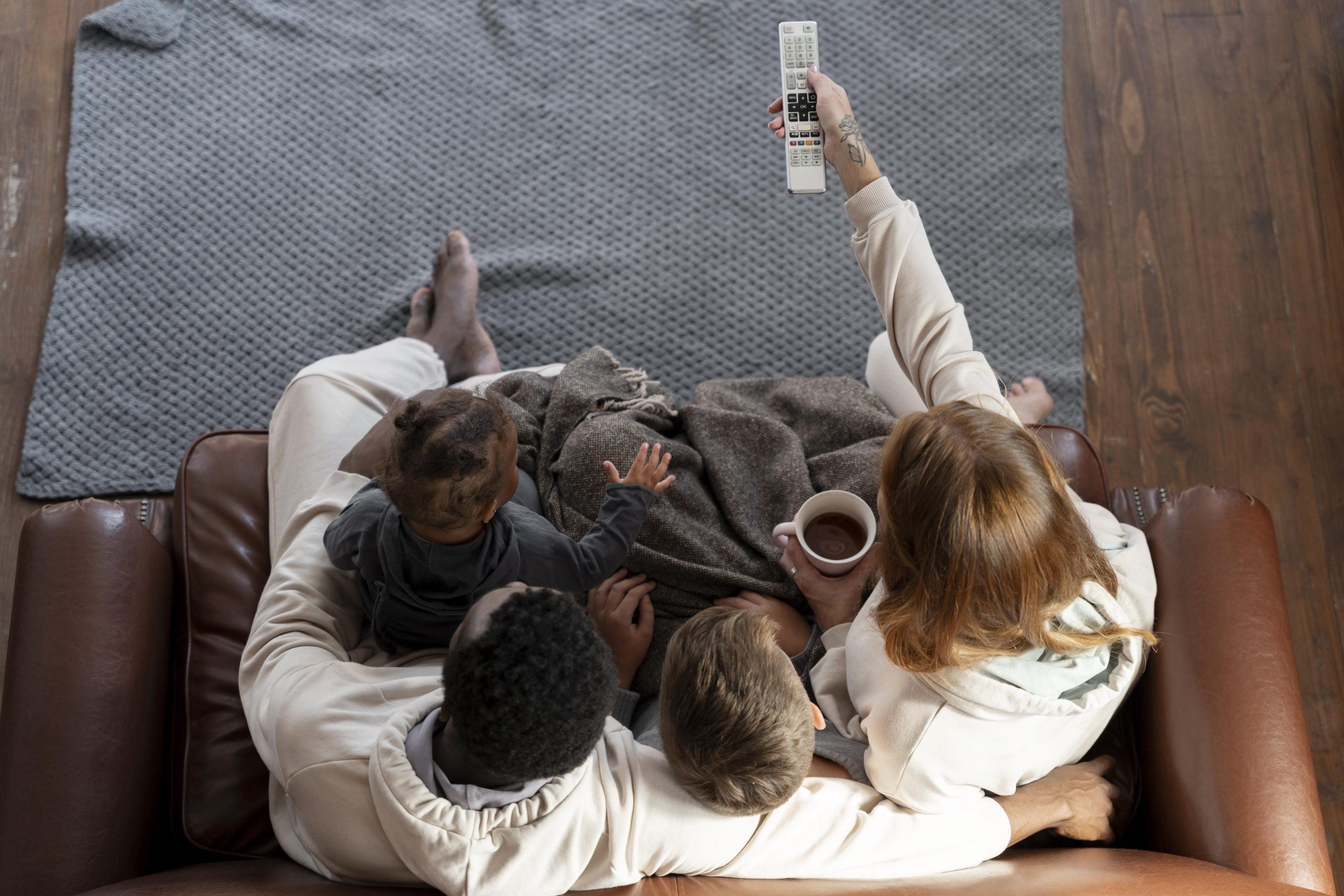 Ģimene sēž uz dīvāna un skatās televīziju