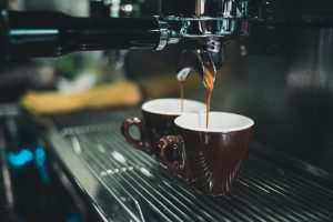 Divas espresso krūzes zem kafijas automāta, kurās tiek gatavota kafija.