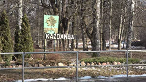 Kazdangas ciema zīme ar ozollapas simbolu meža fonā.