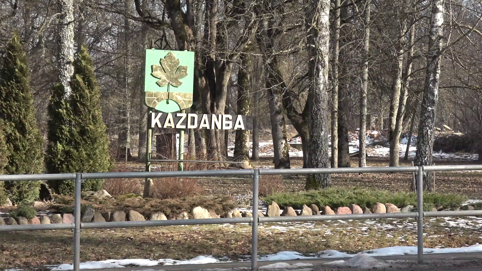 Kazdangas ciema zīme ar ozollapas simbolu meža fonā.