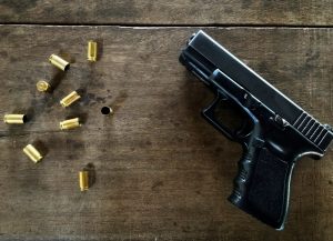 Melnas krāsas pistole un vairākas izšautas patronu čaulītes uz koka virsmas