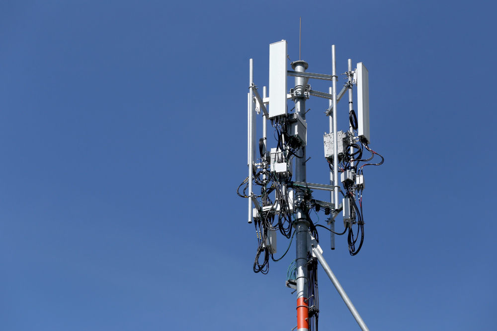 Mobilā sakaru torņa antenas ar kabeļiem, kas nodrošina 4G un 5G pārraides, uz zilu debesu fona