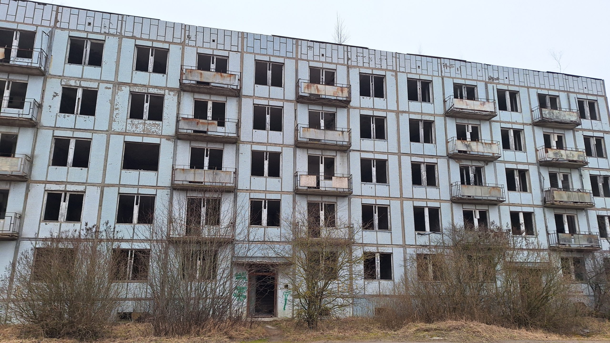Pamesta piecstāvu daudzdzīvokļu ēka ar izsistiem logiem un sarūsējušiem balkoniem