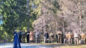 Piemiņas pasākums Īles kaujas vietā, kur cilvēki pulcējas, lai noliktu ziedus un godinātu partizānus.