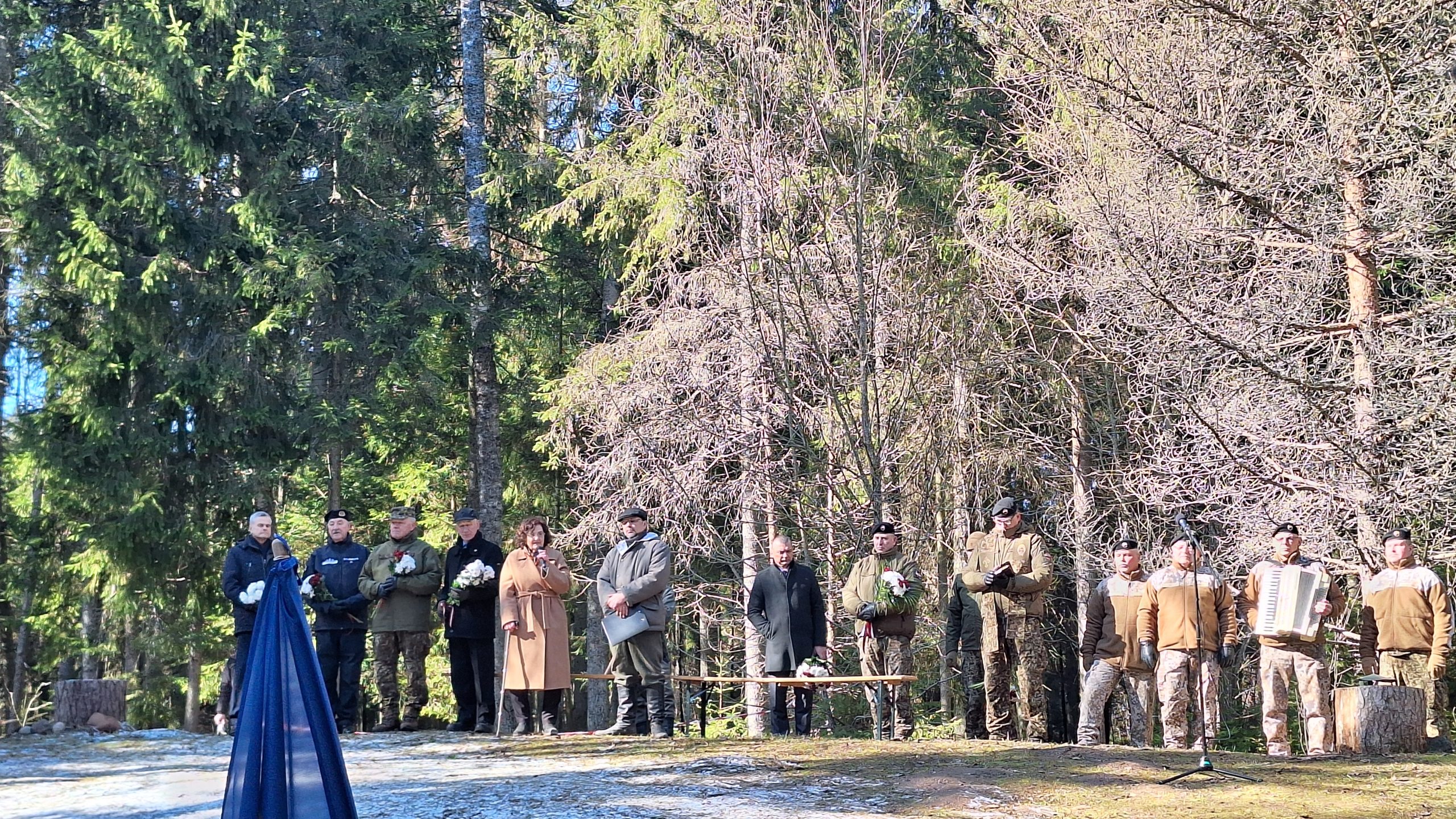 Piemiņas pasākums Īles kaujas vietā, kur cilvēki pulcējas, lai noliktu ziedus un godinātu partizānus.