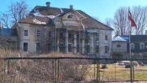 Kaucmindes muiža atjaunošanas procesā ar sastatnēm un Latvijas karogu priekšplānā