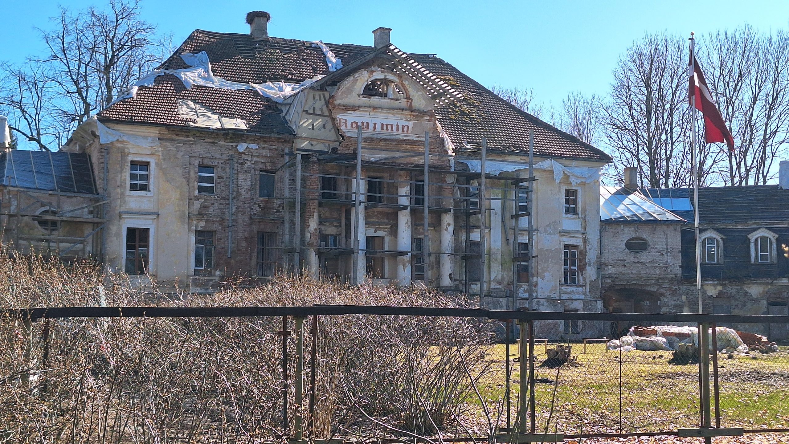 Kaucmindes muiža atjaunošanas procesā ar sastatnēm un Latvijas karogu priekšplānā