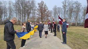 Cilvēki ar Latvijas un Ukrainas karogiem piedalās piemiņas pasākumā brīvā dabā.