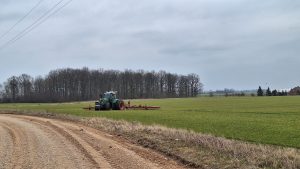 Traktors strādā laukā pie zemes ceļa zem mākoņainām debesīm