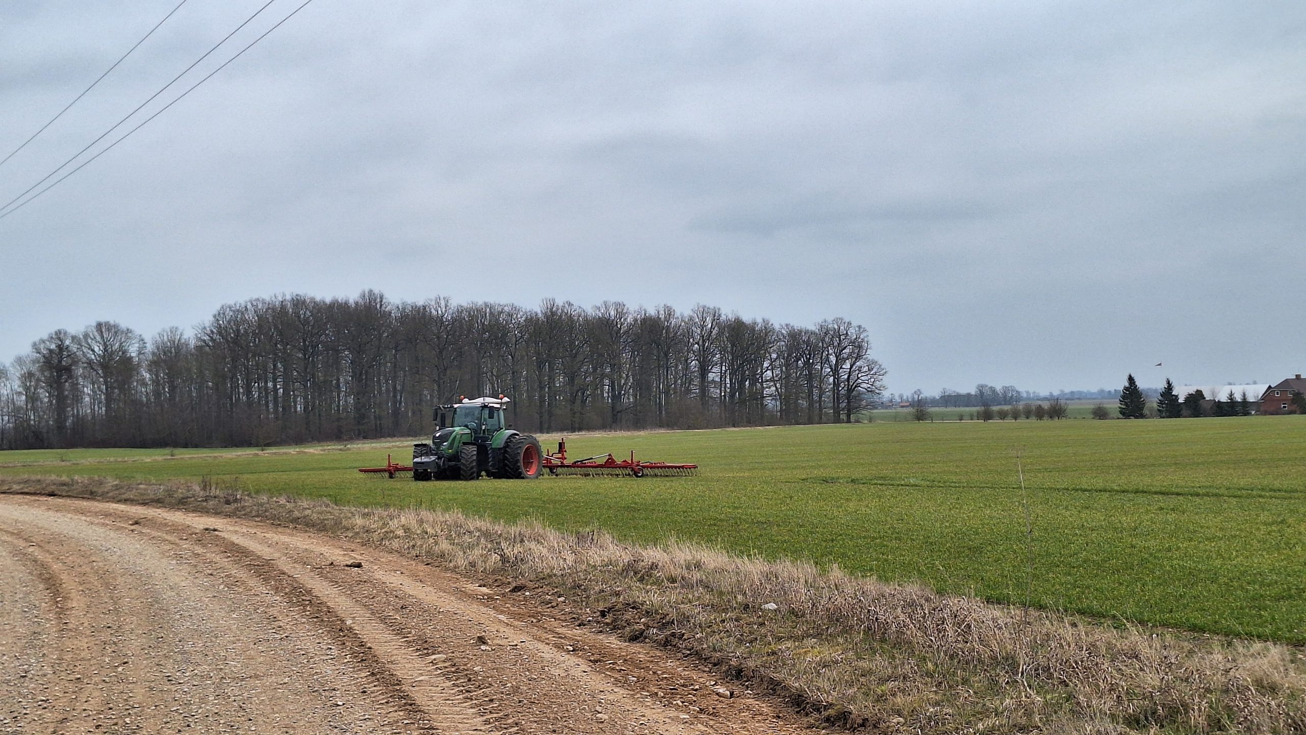 Traktors strādā laukā pie zemes ceļa zem mākoņainām debesīm