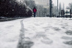 Ziemaina iela ar sniega pārslām un cilvēku sarkanā jakā tālumā