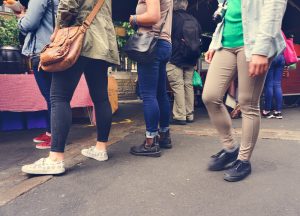 Cilvēki dažādās drēbēs, stāvot rindā pie ielu ēdināšanas stenda, redzami no vidukļa uz leju