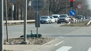 Apgāzies elektroskrejritenis uz ceļa saliņas pie luksofora ar intensīvu satiksmi fonā