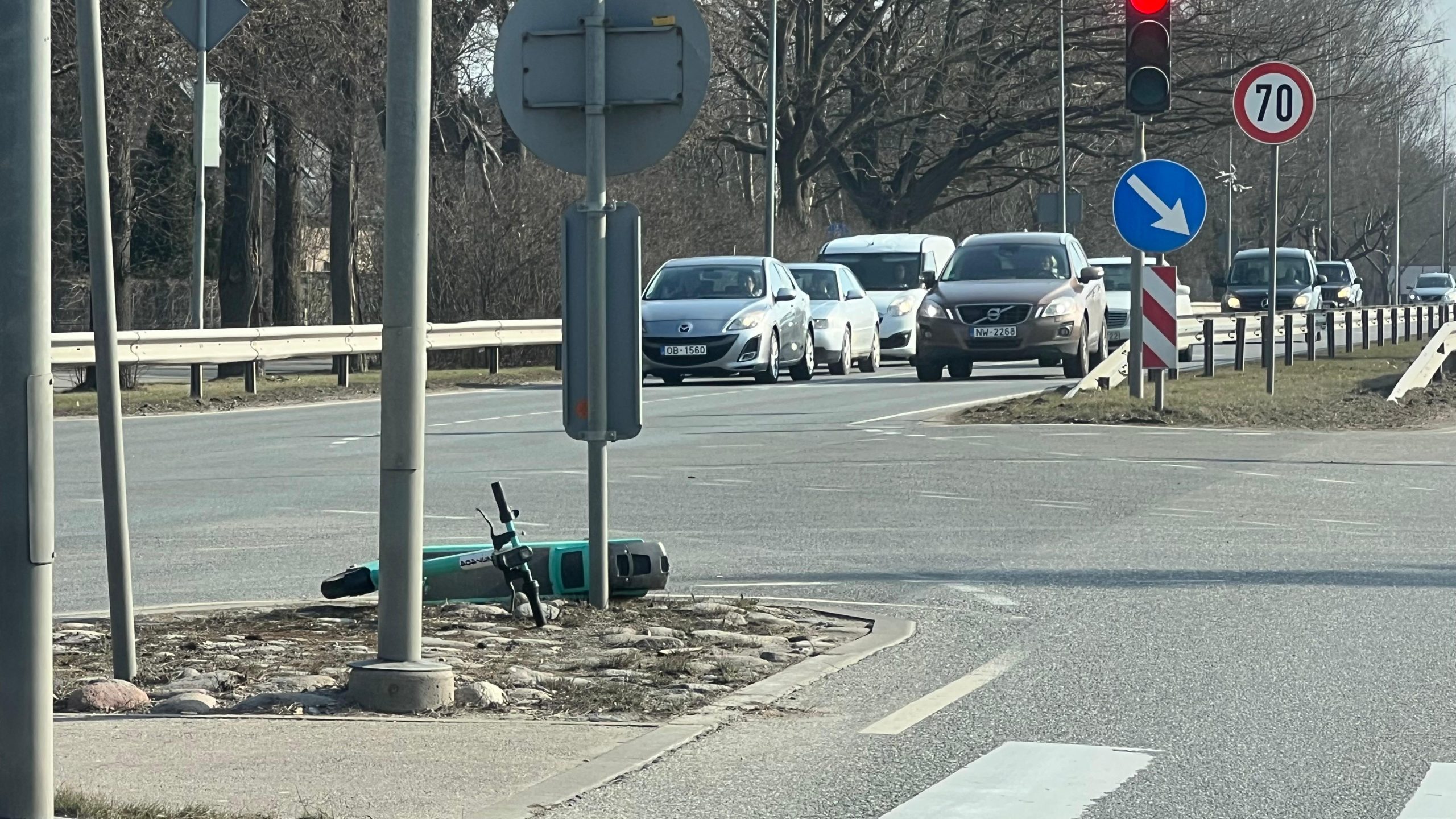 Apgāzies elektroskrejritenis uz ceļa saliņas pie luksofora ar intensīvu satiksmi fonā