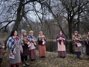 Sievietes tautastērpos sagaida pavasara saullēktu pie ezera.