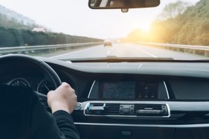 Autovadītājs tur stūri, braucot pa šoseju saulainā dienā