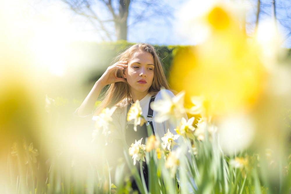 Jauna sieviete pavasarī starp ziedošām narcisēm, sapņainā un gaišā noskaņā