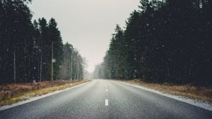 Tukšs, slapjš ceļš, ko ieskauj mežs, vieglā snigšanā ziemīgā dien