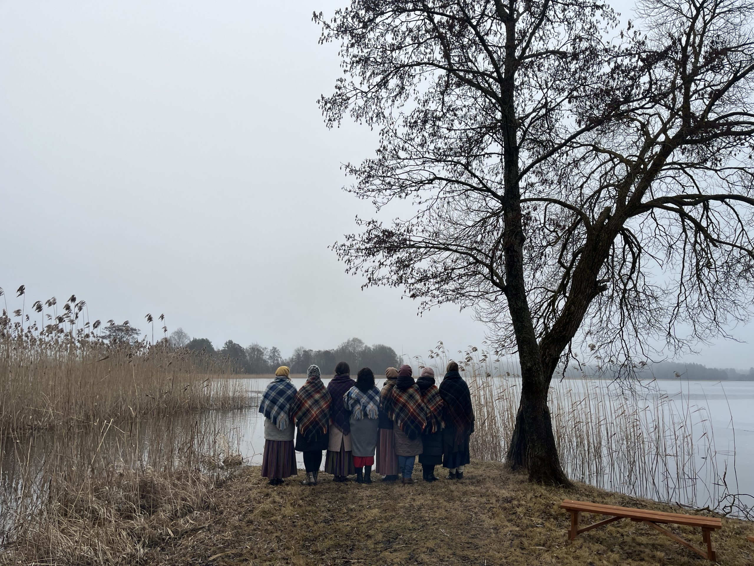 Sievietes tautastērpos sagaida pavasara saullēktu pie ezera.