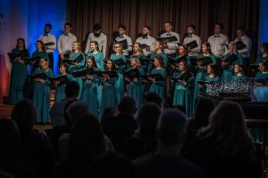 Koris "Pie upes" dzied jubilejas koncertā, tērpti zaļos tērpos.