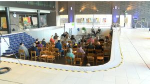 Konference vai diskusija neparastā vietā – sausa baseina telpā ar skatītājiem un runātājiem uz skatuves.