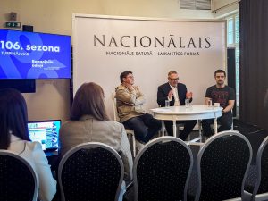 Trīs vīrieši pie apaļa galda preses konferencē, fonā uzraksts Nacionālais un ekrāns ar sezonas informāciju
