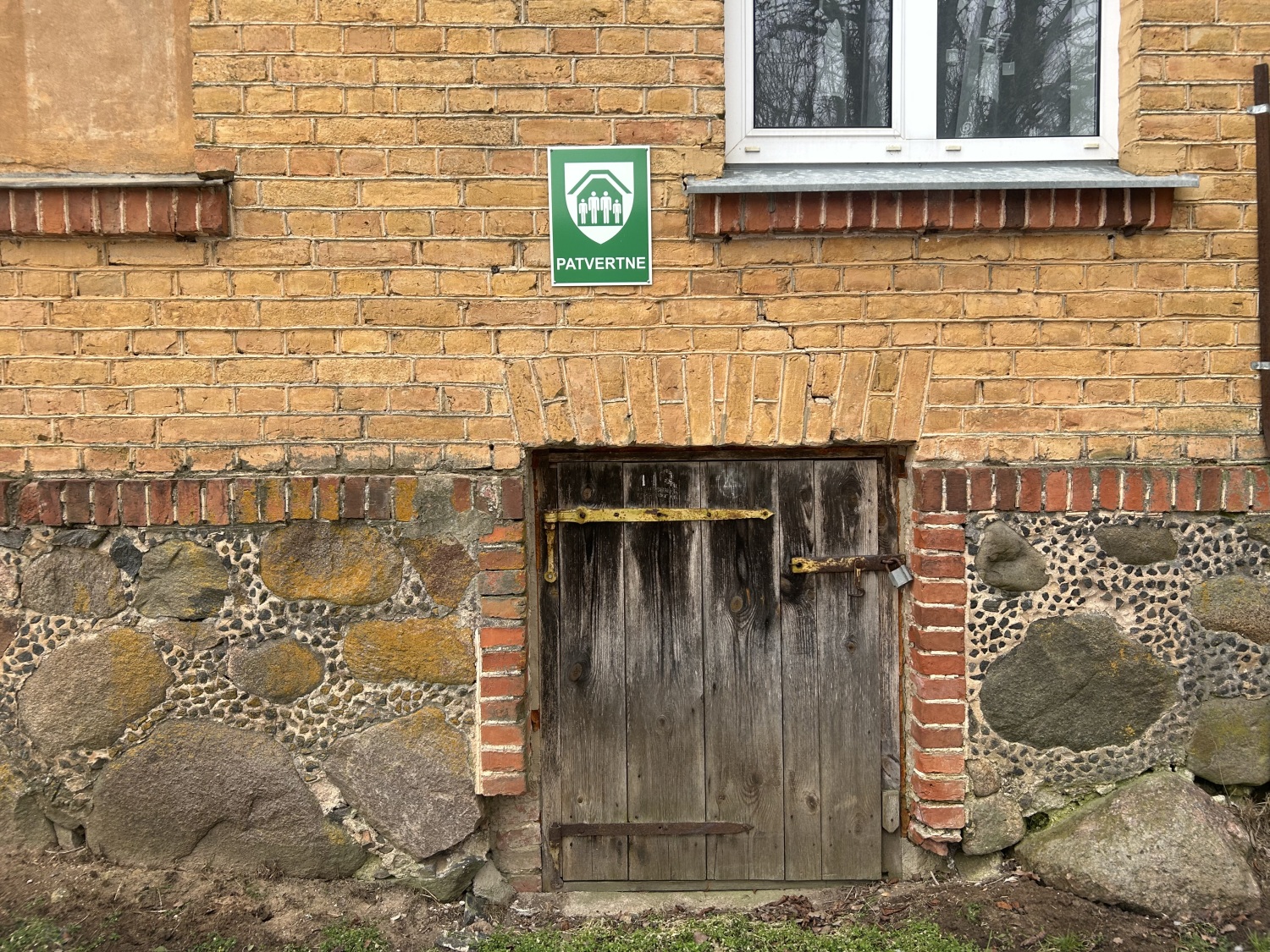 Ķieģeļu ēka ar patvertnes zīmi virs vecām koka durvīm