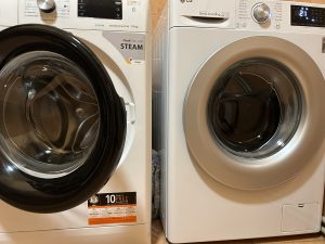 Divas veļas mazgājamās mašīnas – Whirlpool un LG – novietotas blakus vannasistabā